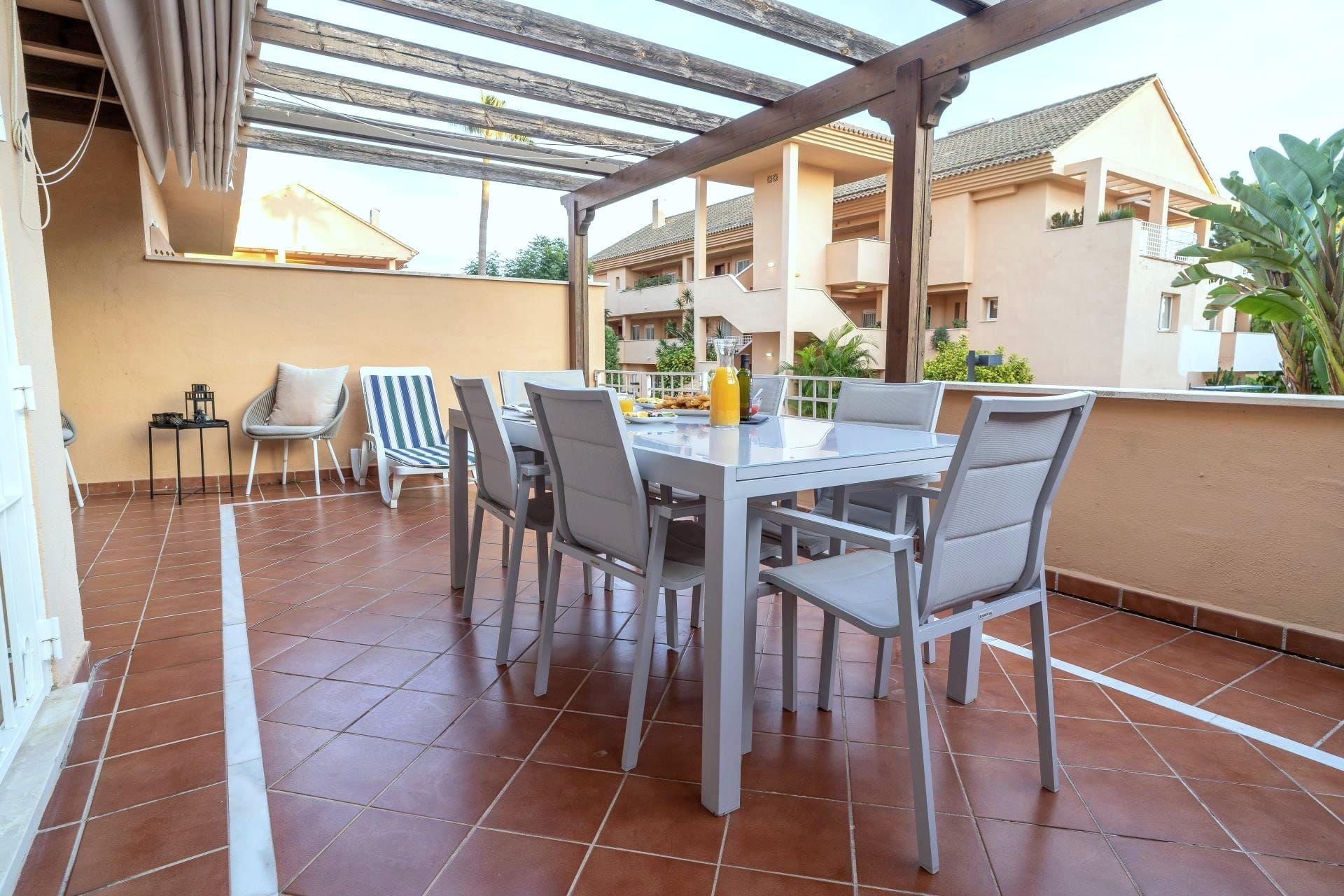 Covered terrace with a dining table, sun loungers and a view of the gardens